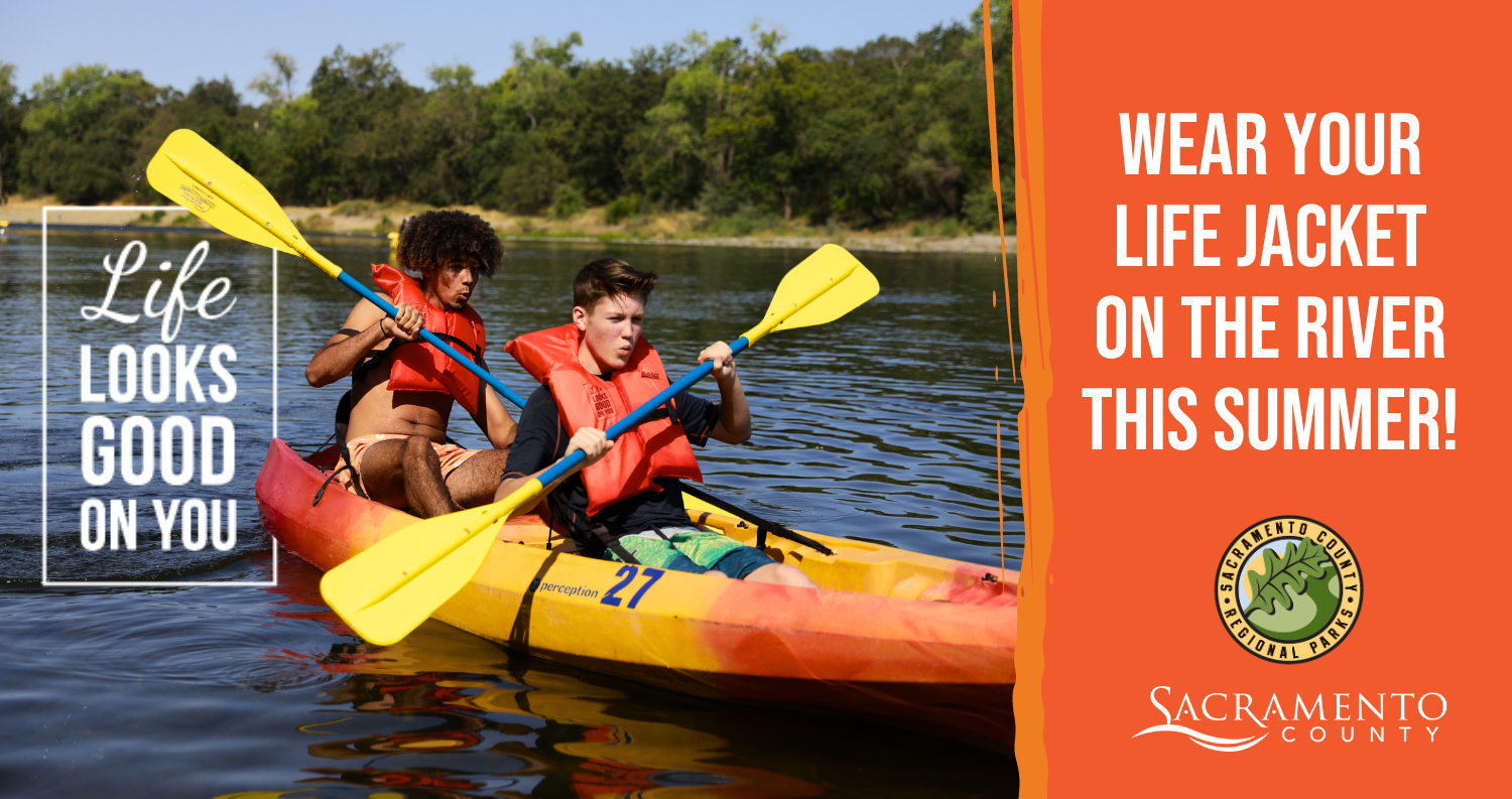 Two individuals paddle a kayak on a river, both wearing orange life jackets. Text overlay encourages wearing life jackets on the river this summer.